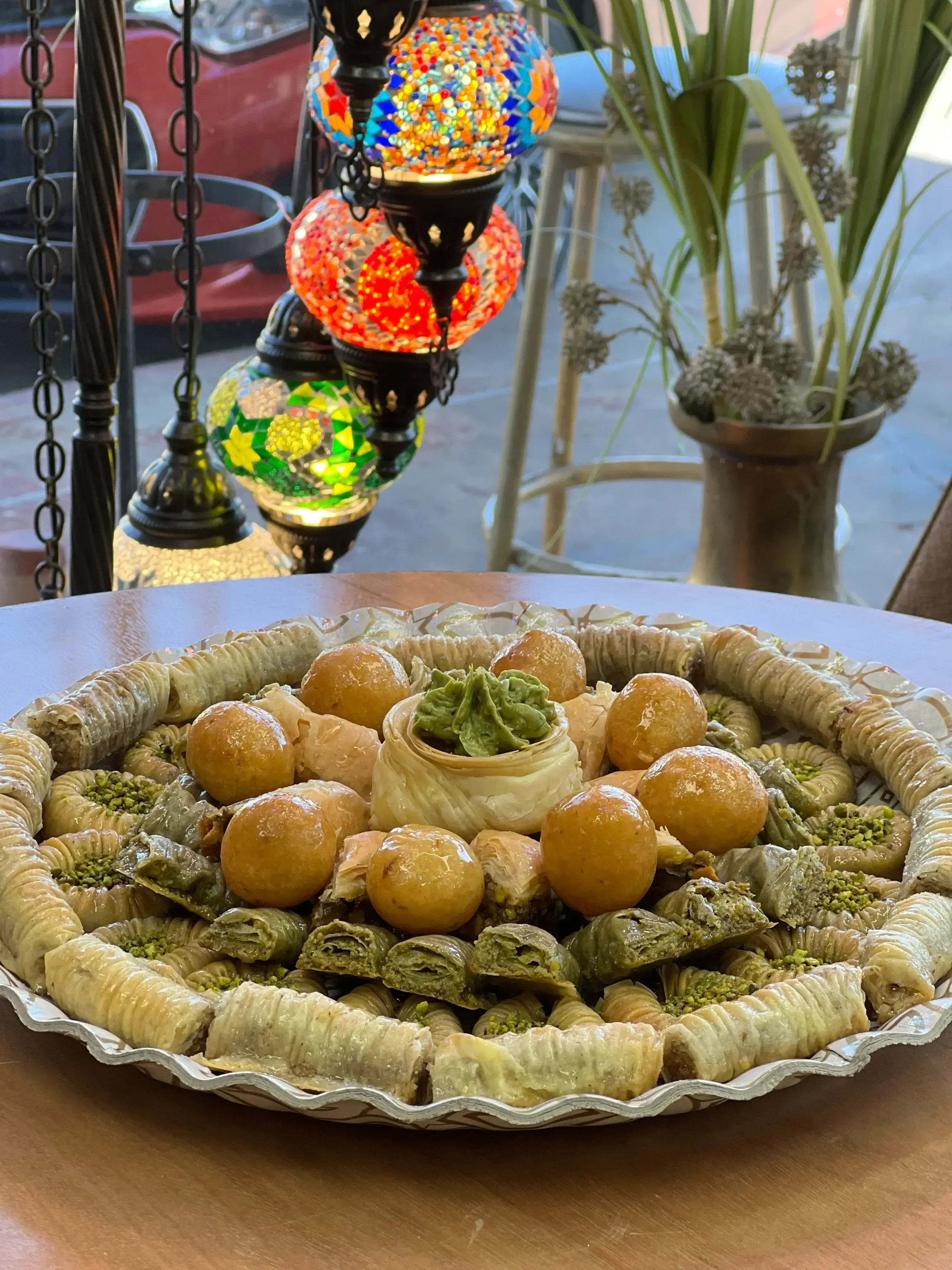 A large oval platter of mixed Iraqi baklava and bird's nest pastries in the bakery window